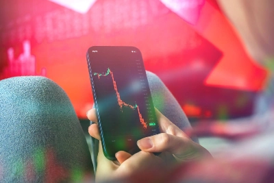 una persona sosteniendo un smartphone que despliega un gráfico financiero con una fuerte tendencia bajista en rojo. El fondo desenfocado refuerza la sensación de pérdida o caída del mercado