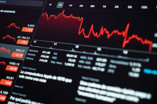 Primer plano de una pantalla digital que muestra gráficos financieros en rojo con una fuerte tendencia bajista, junto a indicadores económicos negativos que sugieren pérdidas en el mercado.