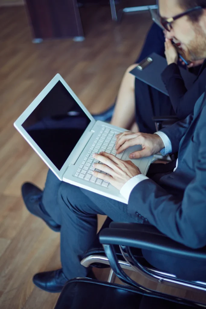 Vista de plano medio de un ejecutivo en traje escribiendo en una computadora portátil durante una reunión de negocios corporativa.